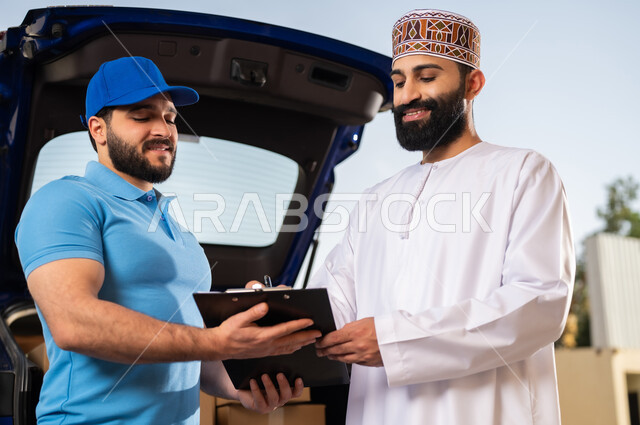 خدمات الشحن ذات الجودة العالية, عمليات الشراء أونلاين, مفهوم التسوق الالكتروني, شاب عربي خليجي عماني يرتدي الدشداشة و الكمة يقوم بالتوقيع على أوراق و مستندات للتأكيد على استلام الطرد، مندوب يقوم بتوصيل طلبات الزبائن