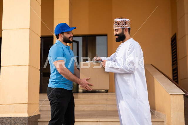 مفهوم التسوق الالكتروني, شاب عربي خليجي عماني يرتدي الدشداشة و الكمة يقوم بالتوقيع على أوراق و مستندات للتأكيد على استلام الطرد، عملية توصيل الطلبات للزبائن، خدمات الشحن ذات الجودة العالية