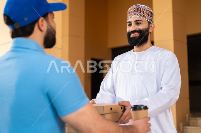 عملية شراء الكترونية، خدمات التوصيل السريع للمأكولات و المشروبات الساخنة, شاب عربي خليجي عماني يرتدي الدشداشة و الكمة يقوم باستلام المشتريات, مفهوم التسوق الالكتروني و الطلبات أونلاين