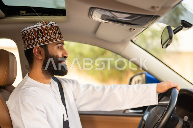 الالتزام بوضع حزام الأمان, مفهوم القيادة الآمنة, صورة مقربة لسائق عربي خليجي عماني يرتدي الدشداشة و الكمة يمسك المقود بيده و يقود السيارة بتعابير السعادة و السرور, خدمات النقل و التوصيل في عمان