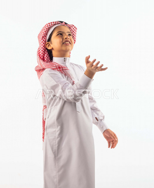 White background of a smiling and beautiful Saudi Gulf young boy, flying up in the balloon with different facial and hand gestures indicating happiness, Portrait of a happy Saudi Gulf child wearing traditional Saudi costume, Celebrating Happy Eid Al-Fitr,