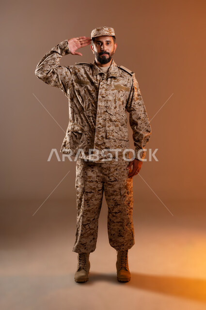 الدفاع عن الوطن، القوات المسلحة السعودية، الجيش العربي السعودي، بورتريه لرجل عربي سعودي خليجي يرتدي الزي العسكري يقف باستقامة وانضباط يؤدي التحيه العسكريه، ايماءات وجه تدل على التحيه،  صورة الجسم بالطول الكامل، خلفية برتقاليه