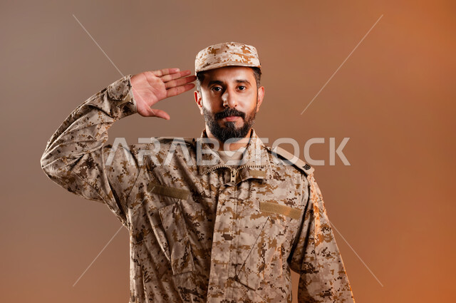 الدفاع عن الوطن، القوات المسلحة السعودية، الجيش العربي السعودي، بورتريه لرجل عربي سعودي خليجي يرتدي الزي العسكري يقف باستقامة وانضباط يؤدي التحيه العسكريه، ايماءات وجه تدل على التحيه،  صورة الجسم بالطول الكامل، خلفية برتقاليه