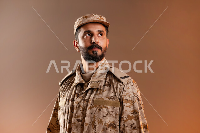 Rapid Intervention Forces, standing upright, prepared and disciplined, portrait of a Saudi Gulf Arab man wearing a military uniform standing in anticipation of a danger coming from afar (Falcon Eyes), maintaining security and safety, Saudi Armed Forces, orange background