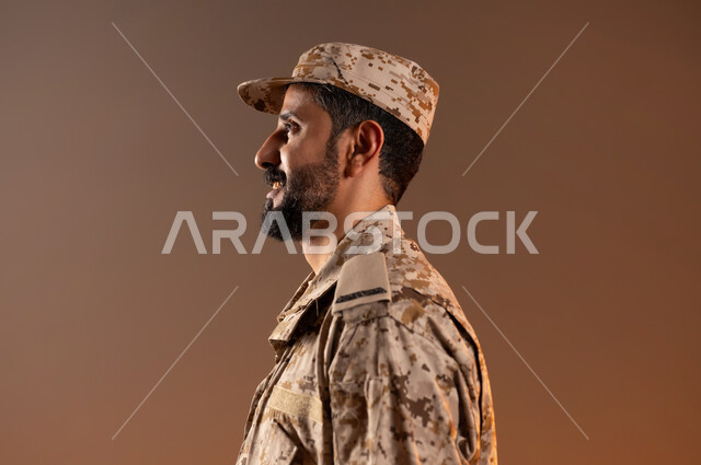 الدفاع عن الوطن، القوات المسلحة السعودية، الجيش العربي السعودي، بورتريه لرجل عربي سعودي خليجي يرتدي الزي العسكري يقف بالطول الجانبي باستقامة وانضباط، ايماءات وجه تدل على الجديه، صورة الجسم بالطول الكامل، خلفية برتقاليه