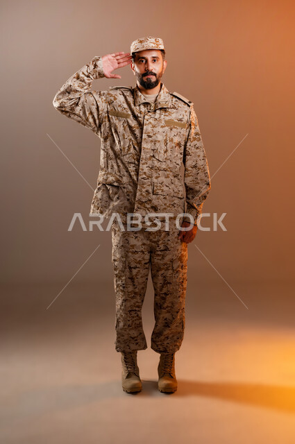 الدفاع عن الوطن، القوات المسلحة السعودية، الجيش العربي السعودي، بورتريه لرجل عربي سعودي خليجي يرتدي الزي العسكري يقف باستقامة وانضباط يؤدي التحيه العسكريه، ايماءات وجه تدل على التحيه،  صورة الجسم بالطول الكامل، خلفية برتقاليه
