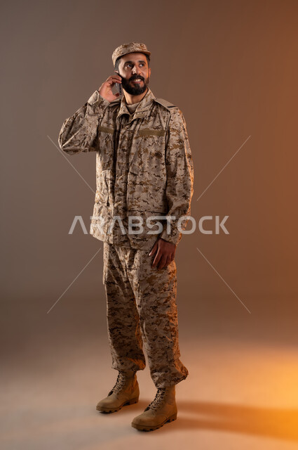 Rapid Intervention Forces, standing upright, prepared and disciplined, portrait of a Saudi Gulf Arab man wearing a military uniform, pointing with his hand behind his ear to listen to military orders silently, maintaining security and safety, Saudi Armed Forces, orange background