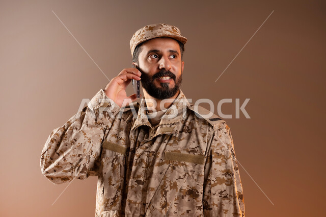 قوات التدخل السريع، الوقوف باستقامة واستعداد وانضباط، بورتريه لرجل عربي خليجي سعودي يرتدي الزي العسكري يشير بيده خلف أذنه للاستماع الى الاوامرالعسكريه بانصات، الحفاظ على الأمن والأمان، القوات المسلحه السعوديه، خلفيه برتقاليه