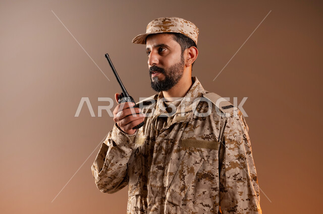 قوات التدخل السريع، الوقوف باستقامة واستعداد وانضباط، بورتريه لرجل عربي خليجي سعودي يرتدي الزي العسكري يمسك بيده جهاز الارسال والاستقبال اللاسلكي، الحفاظ على الأمن والأمان، القوات المسلحه السعوديه، خلفيه برتقاليه