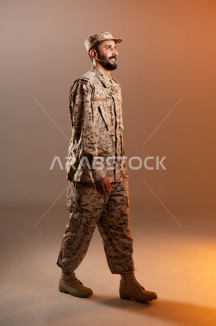الدفاع عن الوطن، القوات المسلحة السعودية، الجيش العربي السعودي، حركات تدل عل الذهاب الى مكان ما، بورتريه لرجل عربي سعودي خليجي يرتدي الزي العسكري يسير باتجاه هدف ما، صورة الجسم بالطول الكامل، خلفية برتقاليه
