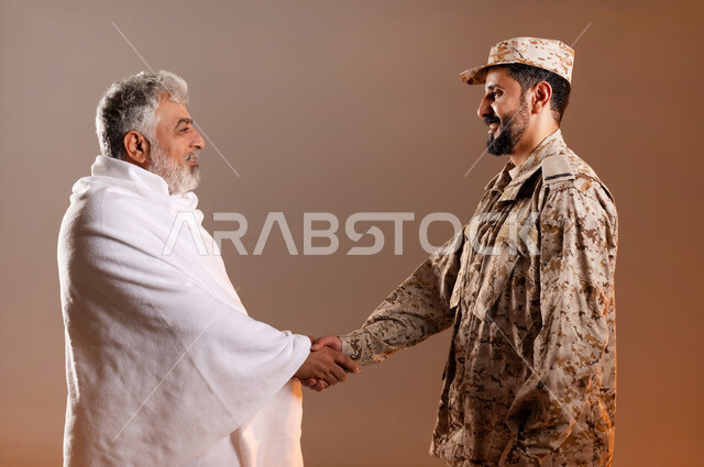 مساعده الحجاج والمعتمرين القادمين الى مكه المكرمه لاداء المشاعر الدينيه، شهامه رجال الامن في خدمه ضيوف الرحمن، بورتريه لرجل عربي خليجي سعودي يرتدي الزي العسكري يقوم بمصافحه رجل كبير بالسن يرتدي ثياب الاحرام تقديرا واحتراما له، خلفيه برتقاليه