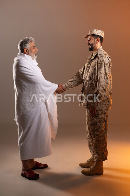 مساعده الحجاج والمعتمرين القادمين الى مكه المكرمه لاداء المشاعر الدينيه، شهامه رجال الامن في خدمه ضيوف الرحمن، بورتريه لرجل عربي خليجي سعودي يرتدي الزي العسكري يقوم بمصافحه رجل كبير بالسن يرتدي ثياب الاحرام تقديرا واحتراما له، خلفيه برتقاليه