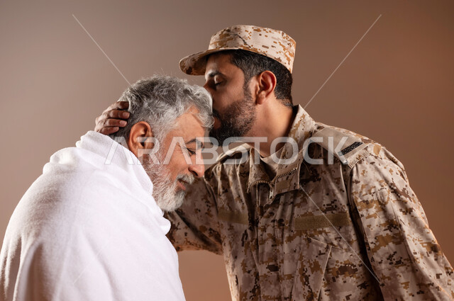 مساعده الحجاج والمعتمرين القادمين الى مكه المكرمه لاداء المشاعر الدينيه، شهامه رجال الامن في خدمه ضيوف الرحمن، بورتريه لرجل عربي خليجي سعودي يرتدي الزي العسكري يقوم بتقبيل رأس رجل كبير بالسن يرتدي ثياب الاحرام تقديرا واحتراما منه، خلفيه برتقاليه