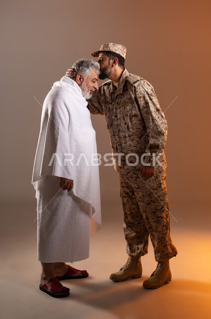 مساعده الحجاج والمعتمرين القادمين الى مكه المكرمه لاداء المشاعر الدينيه، شهامه رجال الامن في خدمه ضيوف الرحمن، بورتريه لرجل عربي خليجي سعودي يرتدي الزي العسكري يقوم بتقبيل رأس رجل كبير بالسن يرتدي ثياب الاحرام تقديرا واحتراما منه، خلفيه برتقاليه