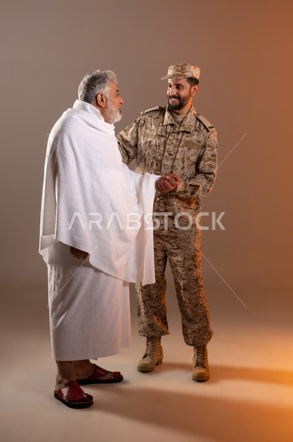 Helping pilgrims and Umrah pilgrims coming to Mecca to perform religious rituals, the gallantry of security personnel serving the guests of God, a portrait of a Saudi Gulf Arab man wearing a military uniform holding the hand of an elderly man wearing Ihram clothes to help him stand and walk, orange background.
