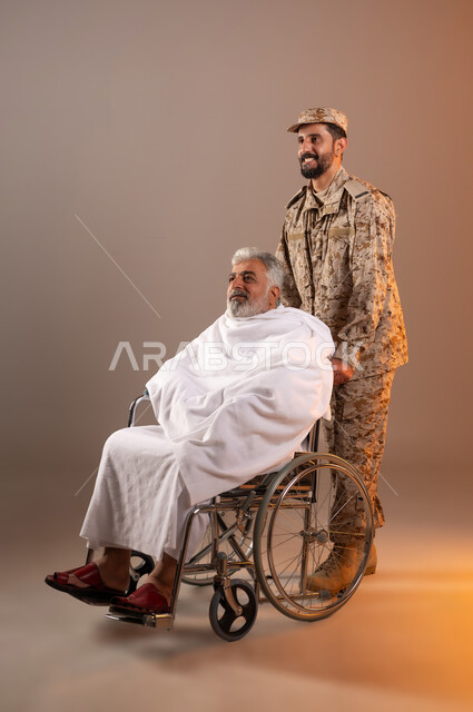 مساعده الحجاج والمعتمرين القادمين الى مكه المكرمه لاداء المشاعر الدينيه، شهامه رجال الامن في خدمه ضيوف الرحمن، بورتريه لرجل عربي خليجي سعودي يرتدي الزي العسكري يقوم بجر الكرسي المتحرك لرجل كبير بالسن يرتدي ثياب الاحرام من ذوي الاحتياجات الخاصه، خلفيه برتقاليه