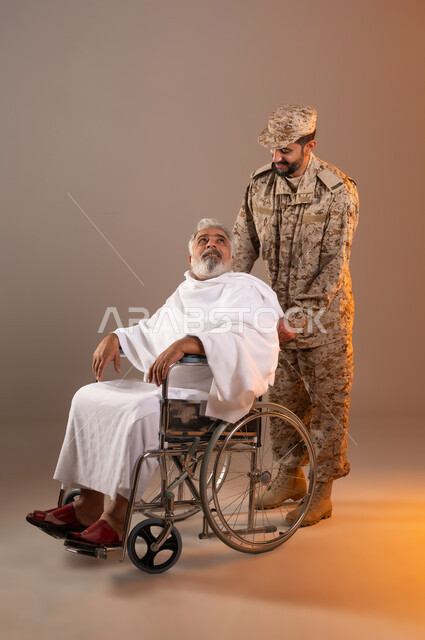 مساعده الحجاج والمعتمرين القادمين الى مكه المكرمه لاداء المشاعر الدينيه، شهامه رجال الامن في خدمه ضيوف الرحمن، بورتريه لرجل عربي خليجي سعودي يرتدي الزي العسكري يقوم بجر الكرسي المتحرك لرجل كبير بالسن يرتدي ثياب الاحرام من ذوي الاحتياجات الخاصه، خلفيه برتقاليه
