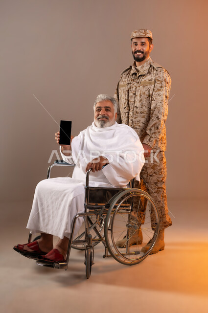 مساعده الحجاج والمعتمرين القادمين الى مكه المكرمه لاداء المشاعر الدينيه، شهامه رجال الامن في خدمه ضيوف الرحمن، بورتريه لرجل عربي خليجي سعودي يرتدي الزي العسكري يقوم بجر الكرسي المتحرك لرجل كبير بالسن يرتدي ثياب الاحرام من ذوي الاحتياجات الخاصه، خلفيه برتقاليه