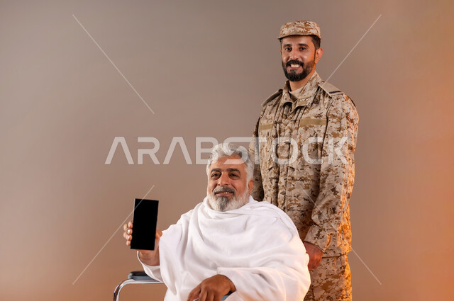مساعده الحجاج والمعتمرين القادمين الى مكه المكرمه لاداء المشاعر الدينيه، شهامه رجال الامن في خدمه ضيوف الرحمن، بورتريه لرجل عربي خليجي سعودي يرتدي الزي العسكري يقوم بجر الكرسي المتحرك لرجل كبير بالسن يرتدي ثياب الاحرام من ذوي الاحتياجات الخاصه، خلفيه برتقاليه
