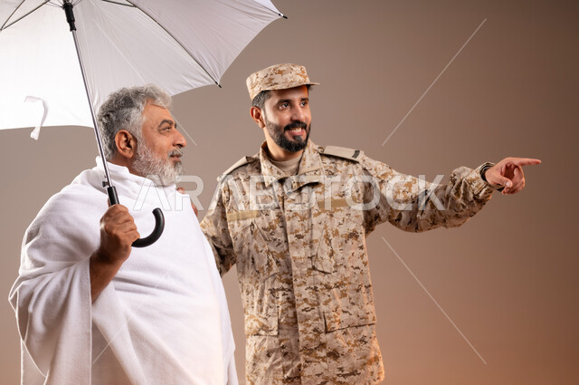 Helping pilgrims and Umrah pilgrims coming to Mecca to perform religious rituals, the gallantry of the security personnel serving the guests of God, a portrait of a Saudi Gulf Arab man wearing a military uniform directing an elderly man wearing Ihram clothes, holding in his hand a white umbrella to protect from the sun’s rays, to reach a place quickly and easily. Orange background