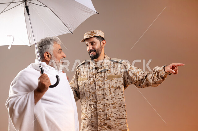 Helping pilgrims and Umrah pilgrims coming to Mecca to perform religious rituals, the gallantry of the security personnel serving the guests of God, a portrait of a Saudi Gulf Arab man wearing a military uniform directing an elderly man wearing Ihram clothes, holding in his hand a white umbrella to protect from the sun’s rays, to reach a place quickly and easily. Orange background