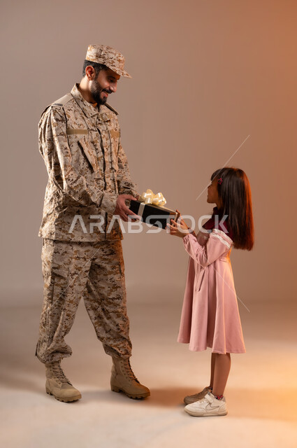 Sharing a wonderful atmosphere of a soldier with his boy, the gallantry of security personnel in dealing with children and bringing joy and happiness to their hearts, a portrait of a Saudi Gulf Arab man wearing a military uniform offering a gift to a young girl wearing a pink dress, the Saudi National Defense Army, orange background