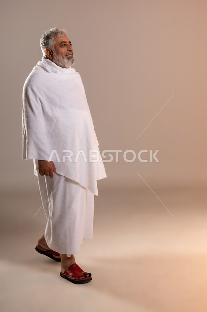 التقرب الى الله بالفرائض والعبادات، بورتريه لرجل عربي خليجي سعودي كبير بالسن يرتدي ثياب الإحرام يسير بسعاده وابتسامه الى مكان ما, اداء مناسك واركان الحج والعمره بيسر وسهوله، خلفيه برتقاليه