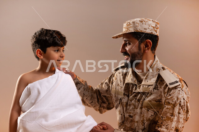 مشاركة اجواء رائعة لعسكري مع صبي ، شهامه رجال الامن بمساعده الحجاج والمعتمرين،  بورتريه لرجل عربي خليجي سعودي يرتدي الزي العسكري يقوم بتعديل ثوب الاحرام لصبي في المسجد الحرام، تأديه مناسك الحج والعمره بيسر وطمأنينه، خلفيه برتقاليه