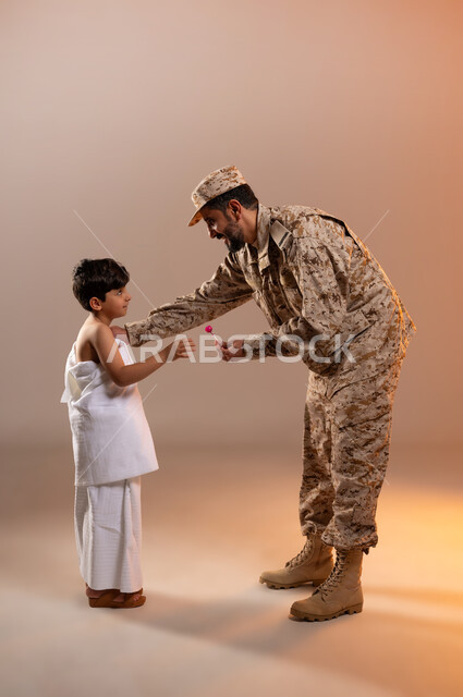 مشاركة اجواء رائعة لعسكري مع صبي ، تقديم الحلوى للاطفال وادخال البهجه والسرور الى قلوبهم، بورتريه لرجل عربي خليجي سعودي يرتدي الزي العسكري يقوم بتقديم حلوى المصاص لصبي يرتدي ثوب الاحرام، تأديه مناسك الحج والعمره بيسر وطمأنينه، خلفيه برتقاليه