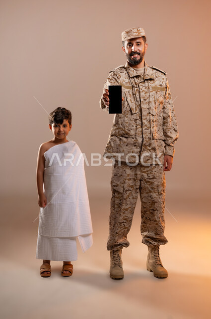 مشاركة اجواء رائعة لعسكري مع صبي ، شهامه رجال الامن بمساعده الحجاج والمعتمرين،  بورتريه لرجل عربي خليجي سعودي يرتدي الزي العسكري يقف بجانب صبي معتمر في المسجد الحرام ويشير بهاتفه المحمول بشاشه سوداء فارغه، تأديه مناسك الحج والعمره بيسر وطمأنينه، خلفيه برتقاليه