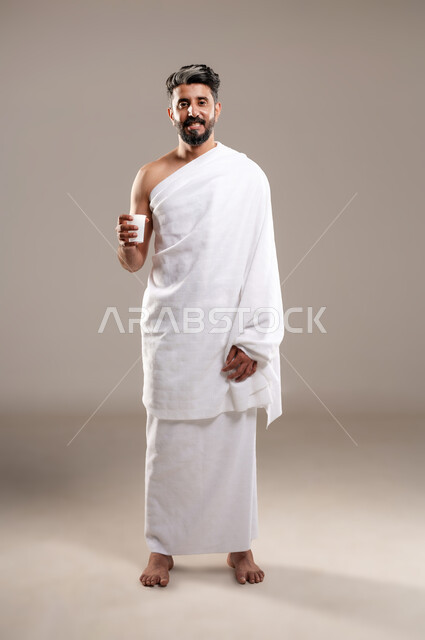 الاستعداد لاداء مناسك الحج والعمره والتقرب الى الله بالاعمال الصالحه، بورتريه لرجل عربي خليجي سعودي يرتدي ثوب الاحرام، الوقوف وشرب ماء زمزم بعد اداء الفريضه والنافله في مكه المكرمه، الركن الخامس من أركان الاسلام لمن استطاع اليه سبيلا، خلفيه رماديه