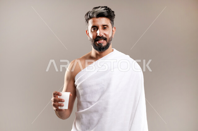 الاستعداد لاداء مناسك الحج والعمره والتقرب الى الله بالاعمال الصالحه، بورتريه لرجل عربي خليجي سعودي يرتدي ثوب الاحرام، الوقوف وشرب ماء زمزم بعد اداء الفريضه والنافله في مكه المكرمه، الركن الخامس من أركان الاسلام لمن استطاع اليه سبيلا، خلفيه رماديه