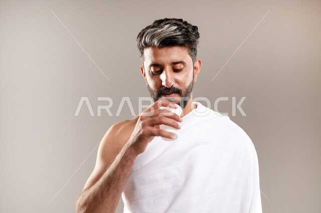 الاستعداد لاداء مناسك الحج والعمره والتقرب الى الله بالاعمال الصالحه، بورتريه لرجل عربي خليجي سعودي يرتدي ثوب الاحرام، الوقوف وشرب ماء زمزم بعد اداء الفريضه والنافله في مكه المكرمه، الركن الخامس من أركان الاسلام لمن استطاع اليه سبيلا، خلفيه رماديه