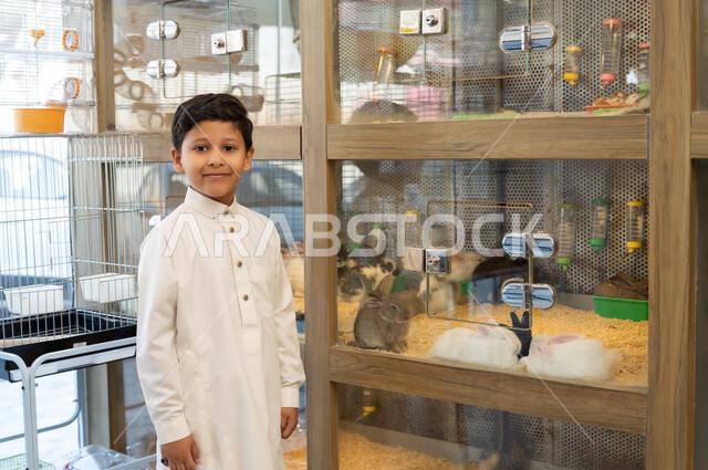 زيارة المحلات الخاصة بشراء الحيوانات الاليفة، مفهوم الرفق بالحيوان والعطف عليه،  صورة مقربة لولد عربي خليجي سعودي يحمل بيده ارنب ابيض اليف