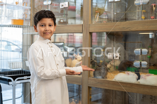 زيارة المحلات الخاصة بشراء الحيوانات الاليفة، مفهوم الرفق بالحيوان والعطف عليه،  صورة مقربة لولد عربي خليجي سعودي يحمل بيده ارنب ابيض اليف