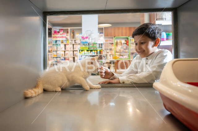 الشغف والاعتناء والاهتمام بالقطط ، قضاء وقت ممتع ومسلي في مشاهدة القط ، صورة مقربة لولد عربي خليجي سعودي يرتدي الثوب التقليدي والشماغ، غرف زجاجية خاصة لحفظ الحيوانات الاليفة، ايماءات السعادة والسرور