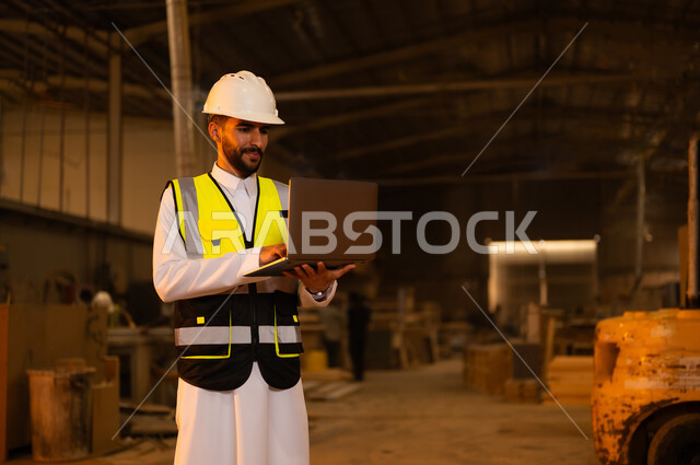 Wooden furniture manufacturing plant, industrial professions and jobs, carpentry workshops in Saudi Arabia, controlling equipment using technology and technology, monitoring and supervising factory machines, a Saudi Arabian Gulf engineer wearing a protective jacket and helmet holding a laptop in his hand
