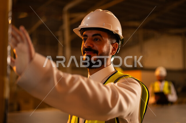 التقدم والتطور التقني في صناعة الخشب، العمل في القطاع الصناعي, صورة مقربة لمهندس عربي خليجي سعودي يرتدي الخوذة وسترة الحماية يعمل على آلة الطباعة الليزرية, اختيار الرسومات والنقوش عبر الحاسب الآلي, معمل تصنيع الأثاث المنزلي