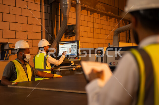 الإشراف على آلات المعمل، ورشات النجارة في السعودية، معمل تصنيع الأثاث الخشبي، مهن ووظائف صناعية، تسجيل وتدوين الملاحظات، صورة مقربة من الخلف لمهندس عربي خليجي سعودي يرتدي سترة وخوذة الحماية يحمل بيده حافظة ورقية