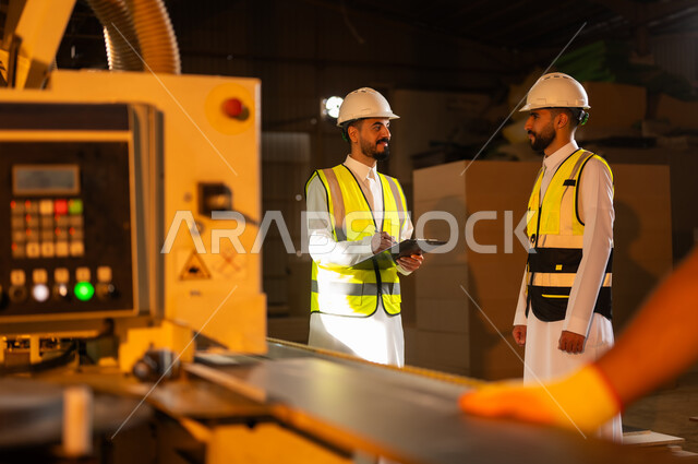 الطباعةعلى القطع الخشبية، التطور والتقدم التقني في صناعة الخشب، العمل في القطاع الصناعي, مهندسين عربيين خليجيين سعوديين يرتديان الخوذة وسترة الحماية يعملان في ورشة نجارة، آلة النقش بالليزر, معمل تصنيع الأثاث المنزلي