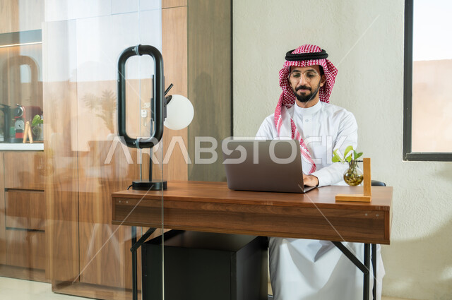 إرسال بريد الكتروني عبر الحاسوب, استخدام التقنيات الحديثة و المتطورة في العمل, مهن و أعمال مكتبية في السعودية, شاب عربي خليجي سعودي يرتدي الثوب التقليدي و الشماغ يجلس داخل المكتب و يقوم بالكتابة على لوحة المفاتيح, التواصل مع العملاء عن بعد