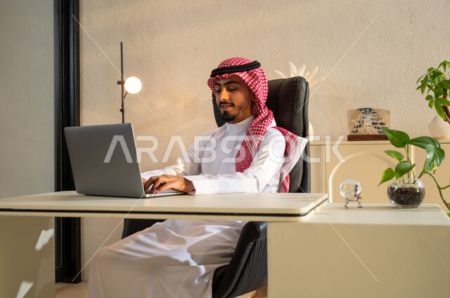 بيئة عمل مريحة في الشركات السعودية، إيماءات الاندماج والتركيز، رجل عربي خليجي سعودي يرتدي الثوب التقليدي والشماغ يقوم بعقد اجتماع عمل عبر الانترنت, تصفح مواقع أخبار السوشال ميديا عبر جهاز الحاسوب, استخدام الأجهزة والتقنيات الحديثة والمتطورة