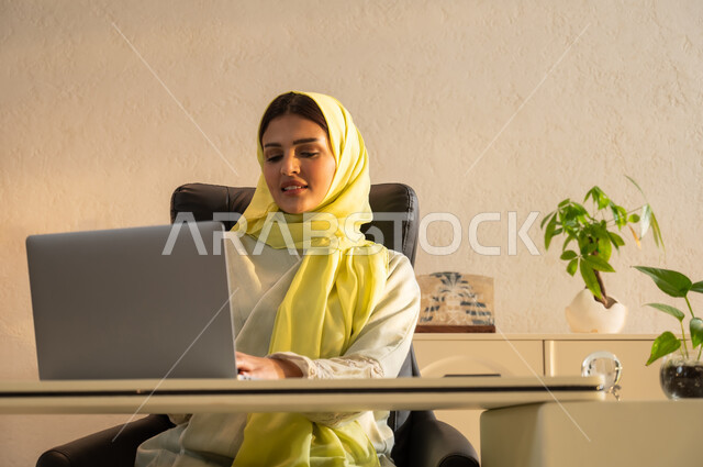 تصفح مواقع أخبار السوشال ميديا عبر جهاز الحاسوب، استخدام الأجهزة والتقنيات الحديثة في إنجاز المهام، بيئة عمل مريحة في الشركات السعودية، إيماءات الاندماج والتركيز، صورة مقربة لشابة عربية خليجية سعودية ترتدي العباية والحجاب تقوم بعقد اجتماع عمل عبر الانترنت
