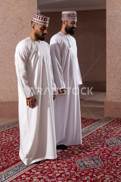العبادة والتقرب إلى الله، إقامة الصلاة على وقتها، أداء الفرائض الدينية الاسلامية، مفهوم أركان الإسلام، صلاة الجماعة لرجلان عربيان خليجيان عمانيان مسلمان يرتديان الكمة والدشداشة داخل مصلى الشركة