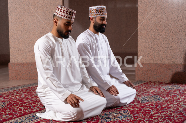أداء الفرائض الدينية الاسلامية، إقامة الصلاة بأوقاتها، مفهوم أركان الإسلام، صلاة الجماعة لرجلان عربيان خليجيان عمانيان مسلمان يرتديان الكمة والدشداشة داخل مصلى الشركة، العبادة والتقرب إلى الله، رفع إصبع السبابة والنطق بالشهادتين