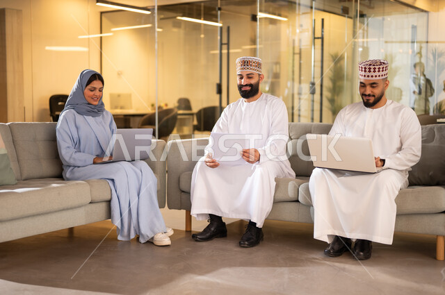 Using modern technical devices to accomplish tasks, the concept of training and developing employees, an Arab Gulf Omani team sitting inside the company headquarters, gestures of joy and happiness, a comfortable environment in Omani companies, administrative professions and jobs in the Sultanate of Oman, exchanging conversations and points of view between colleagues
