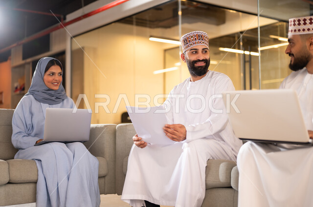 مفهوم تدريب وتطوير الموظفين, فريق عمل عربي خليجي عماني يجلسون داخل مقر الشركة، إيماءات البهجة والسرور، بيئة مريحة في الشركات العمانية، استخدام الأجهزة التقنية الحديثة في إنجاز المهام، مهن ووظائف إدارية في سلطنة عمان، تبادل الأحاديث ووجهات النظر بين الزملاء