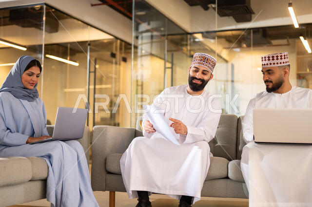 مفهوم تدريب وتطوير الموظفين, فريق عمل عربي خليجي عماني يجلسون داخل مقر الشركة، إيماءات البهجة والسرور، بيئة مريحة في الشركات العمانية، استخدام الأجهزة التقنية الحديثة في إنجاز المهام، مهن ووظائف إدارية في سلطنة عمان، تبادل الأحاديث ووجهات النظر بين الزملاء