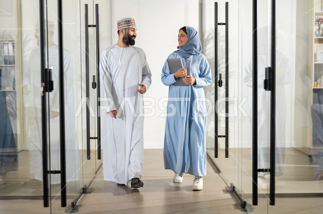 تبادل الخبرات و المهارات, مهن ووظائف إدارية في سلطنة عمان، استخدام الأجهزة التقنية الحديثة في إنجاز المهام، بيئة عمل مريحة، مفهوم الشراكة والتعاون, موظفان عربيان خليجيان عمانيان يسيران داخل مقر الشركة