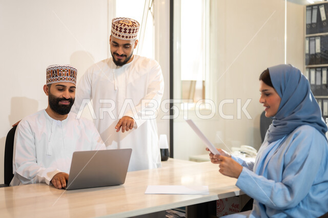 استخدام الأجهزة التقنية الحديثة في إنجاز المهام، بيئة مريحة في الشركات العمانية، تبادل الأحاديث ووجهات النظر بين الزملاء، مهن ووظائف إدارية في سلطنة عمان، إيماءات البهجة والسرور، مفهوم تدريب وتطوير الموظفين, فريق عمل عربي خليجي عماني يقومون باجتماع داخل مكتب